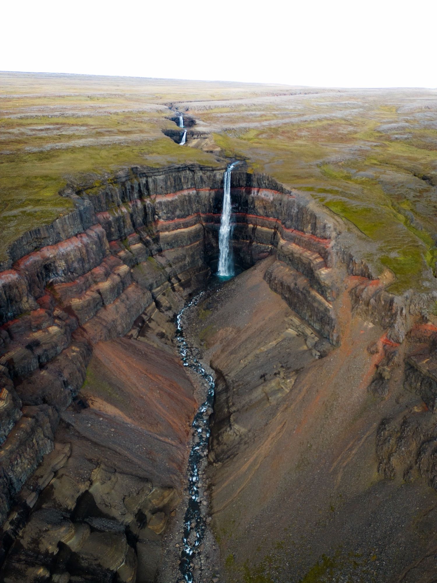 Hengifoss waterfall seen from above, falling past red and black rock layers