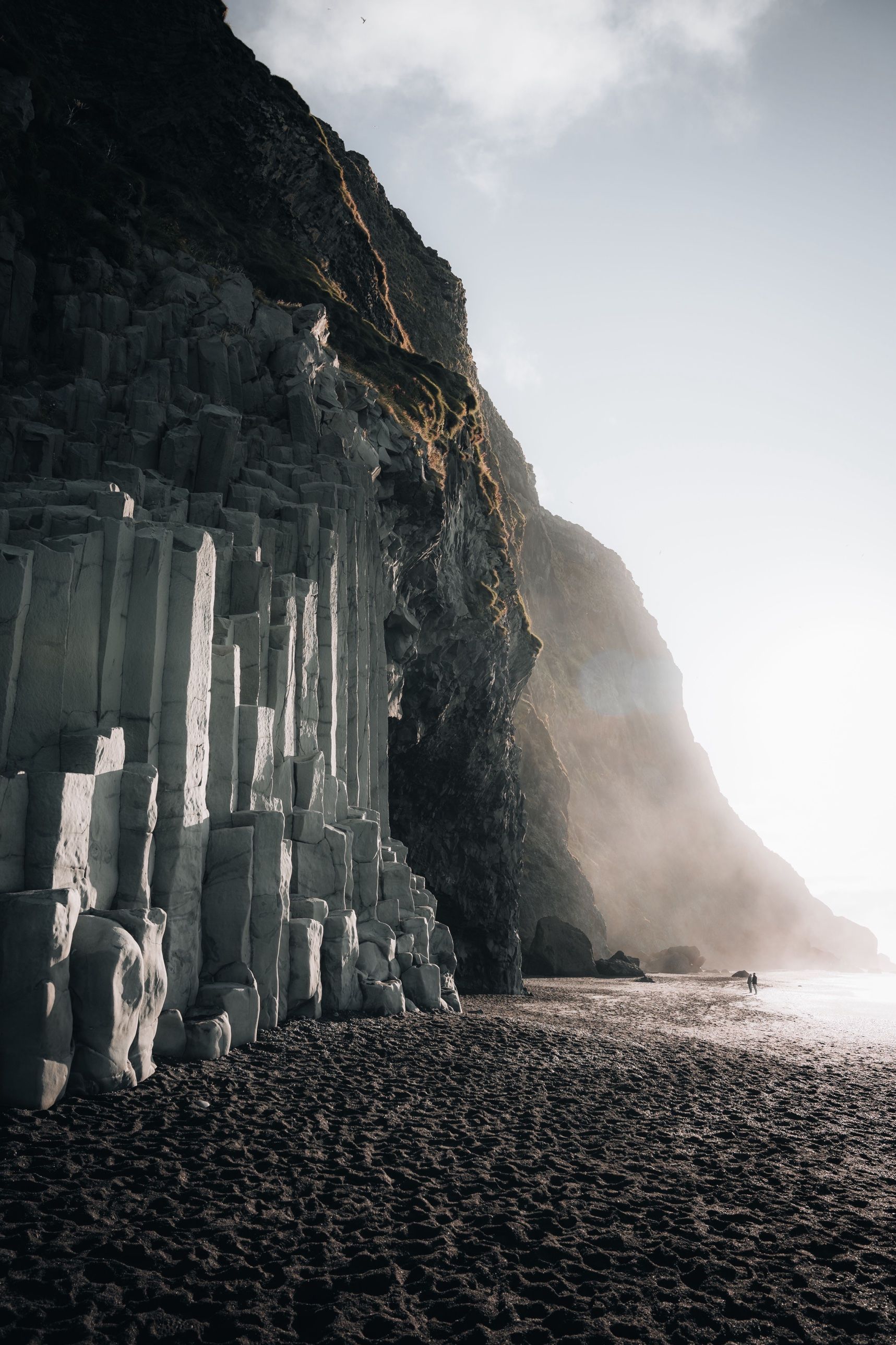Basalt columns at the foot of a cliff on a black sand beach in morning light