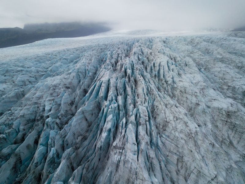 Deep blue crevasses running down a glacier seen from above in mist