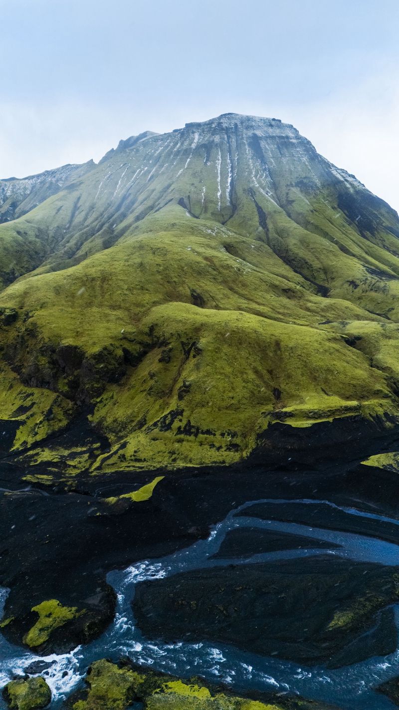 A moss-green mountain above a braided river and black sand