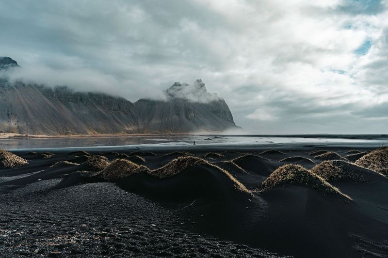 Clouds pouring over Vestrahorn above black dunes and a wet beach