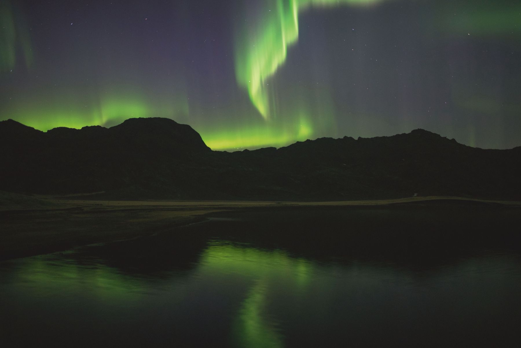 Northern lights over dark mountains reflected in a lake