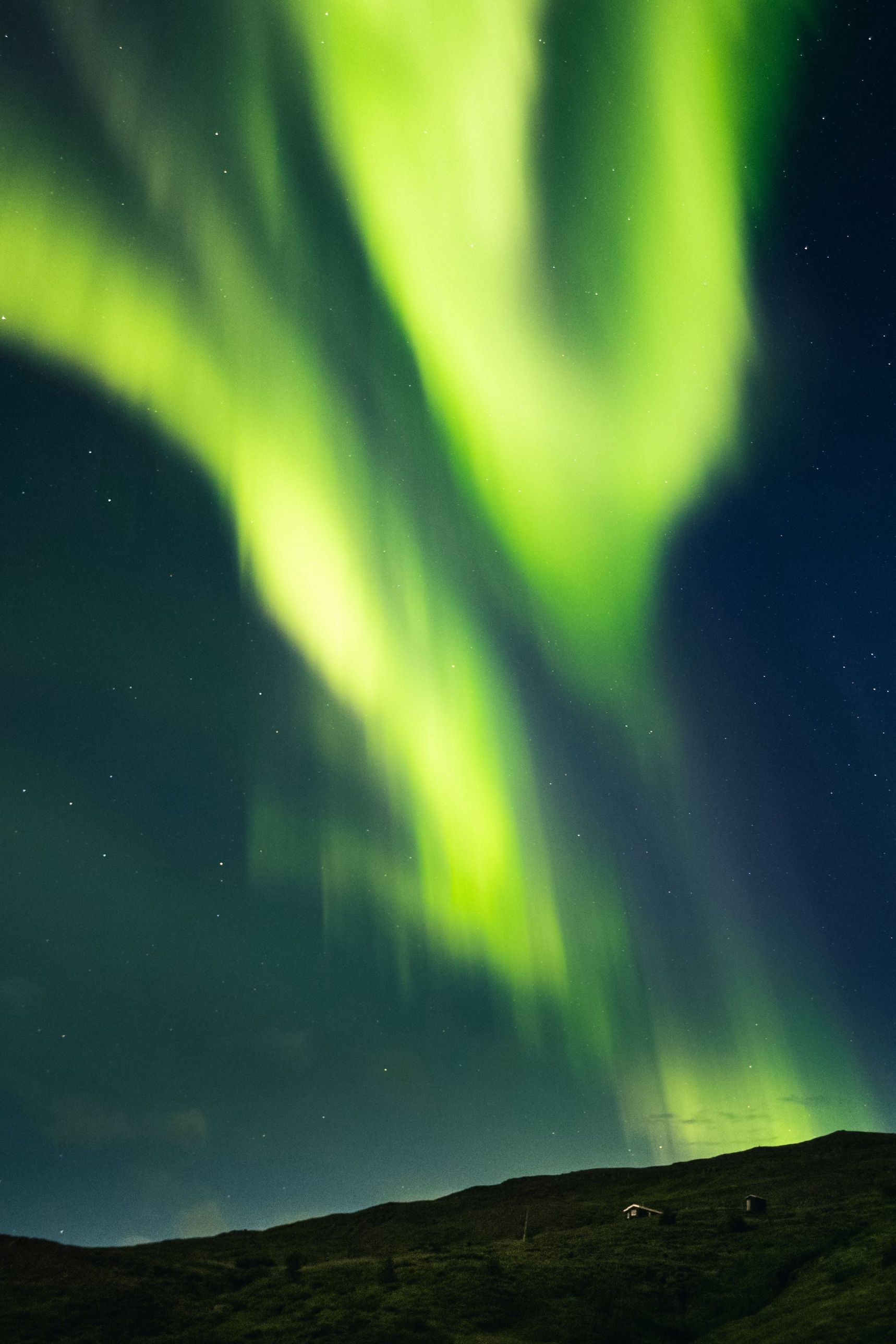 Bright green aurora above a dark hillside with two small cabins