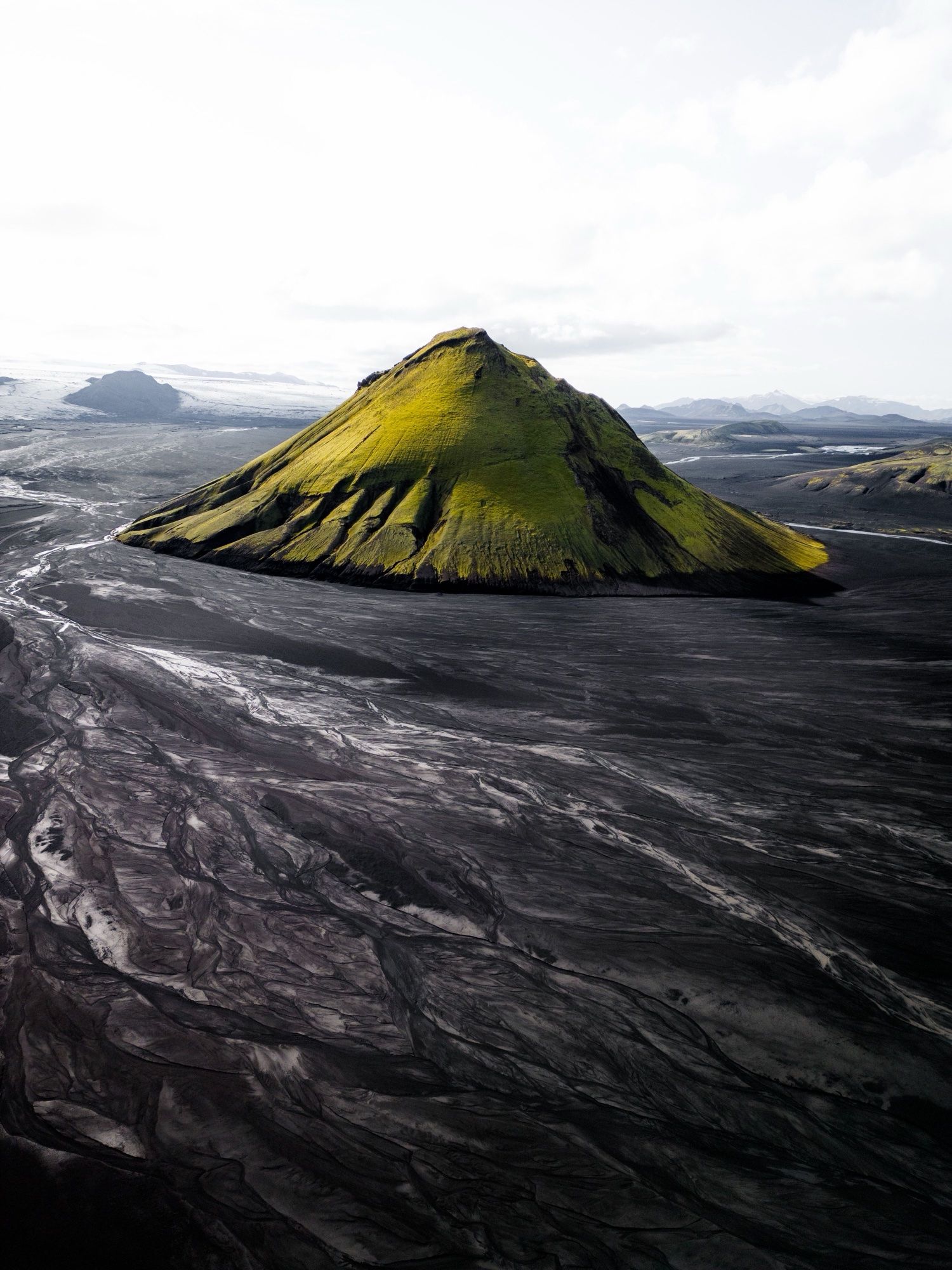 The moss-green cone of Mælifell rising from black sand plains cut by glacial streams